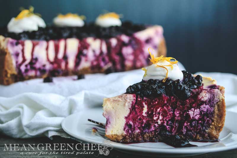 Side photo of a slice of Blueberry Lemon Cheesecake topped with blueberries and fresh whipped cream.