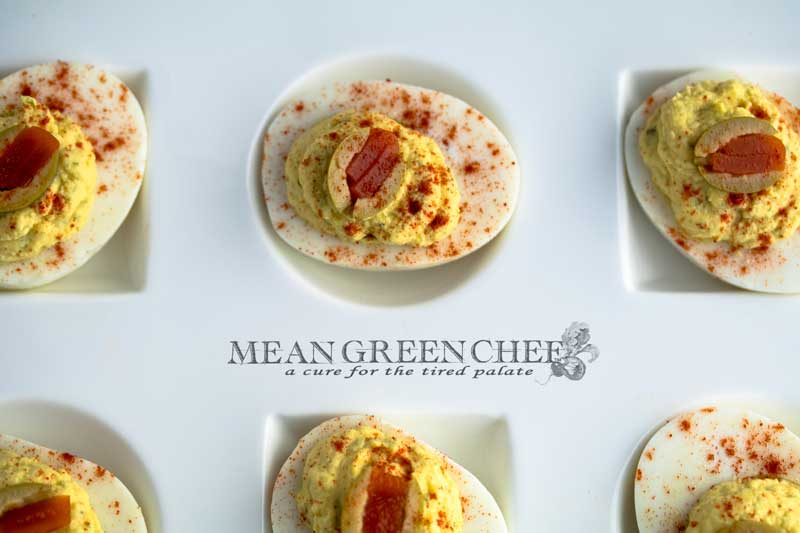 Classic Deviled Eggs on a large with platter with circle and square depressions for the eggs, sitting on a white cotton kitchen towel on an old blue wooden background. Mean Green Chef