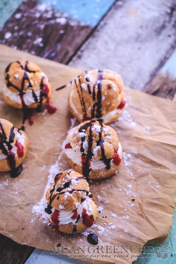 Cream Puffs with Strawberry Coulis shown with a sprinkling of powdered sugar and a drizzle of chocolate sauce