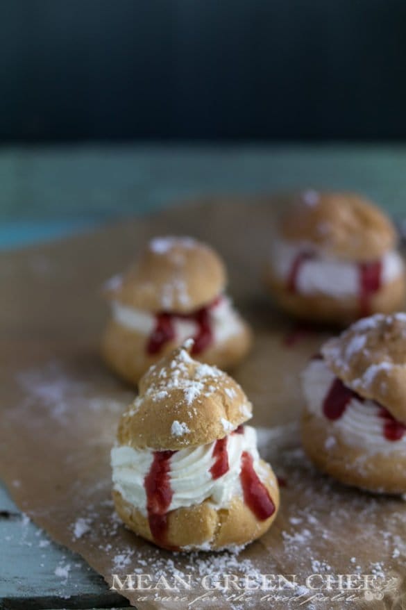 Cream Puffs with Strawberry Coulis shown with a sprinkling of powdered sugar on an old blue wooden background
