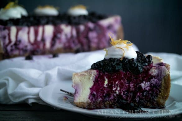 Side photo of a slice of Blueberry Lemon Cheesecake topped with blueberries and fresh whipped cream.