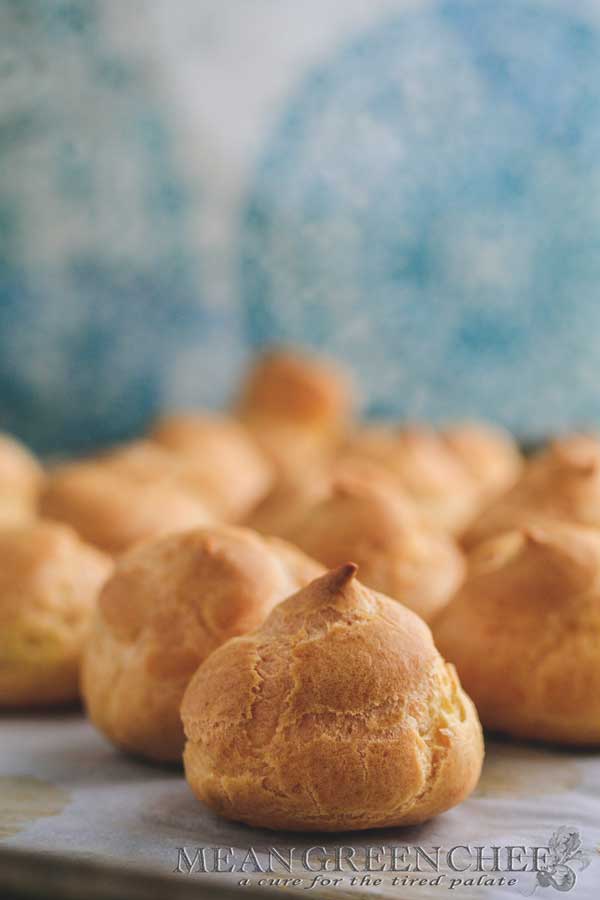 Pate a Choux Pastry baked to a golden brown sitting on a sheet pan lined with parchment paper.
