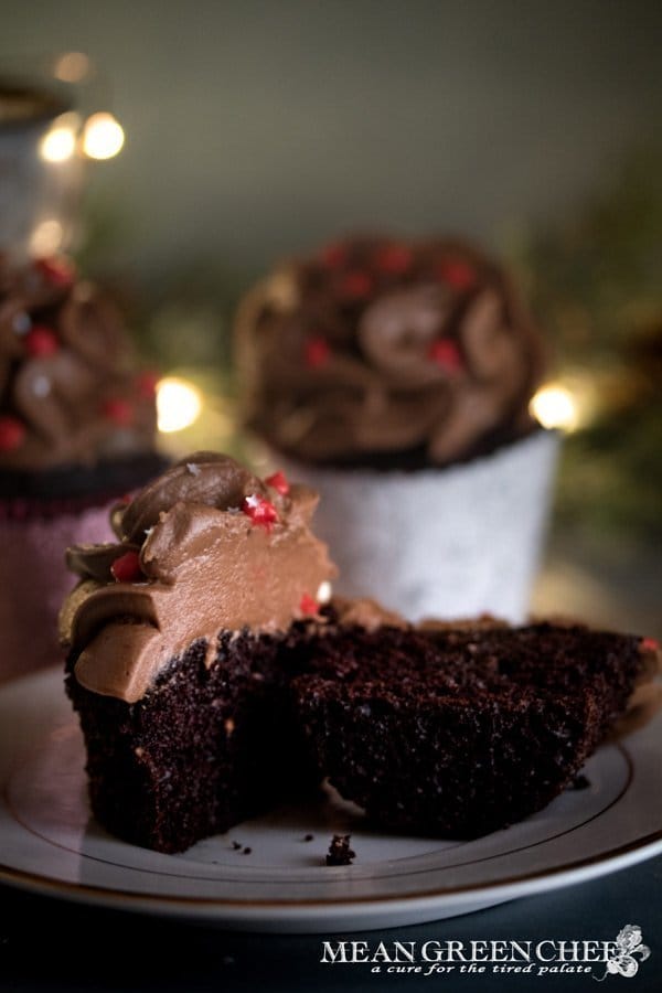 Side photo of Bakery Style Chocolate Cupcake sliced in half and decorated with a high swirl of chocolate frosting red frosting berries and a sprinkle of silver stars in a scalloped gray cupcake wrapper.