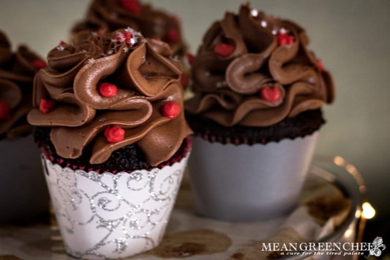 Side photo of Bakery Style Chocolate Cupcakes decorated with a high swirl of chocolate frosting red frosting berries and a sprinkle of silver stars in a scalloped gray and silver cupcake wrappers.