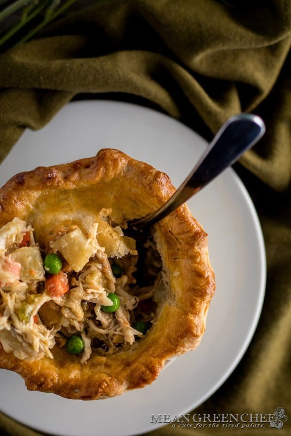Overhead photo of freshly baked chicken pot pie filled with chicken, green peas, carrots, and potatoes. Sitting on a with plate with the top crust broken. Mean Green Chef