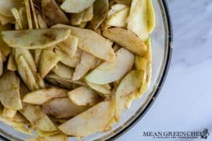 Freshly sliced apples coated with apple pie spice for Caramel Apple Pie in a large glass bowl on a white marbled background. Mean Green Chef