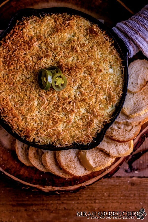 Overhead photo of Jalapeno Popper Dip in a cast iron pan surrounded with toasted sourdough bread rounds. on a rustic wooden background. Mean Green Chef