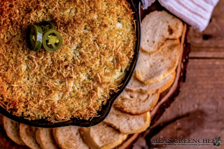 Overhead photo of Jalapeno Popper Dip in a cast iron pan surrounded with toasted sourdough bread rounds. on a rustic wooden background. Mean Green Chef