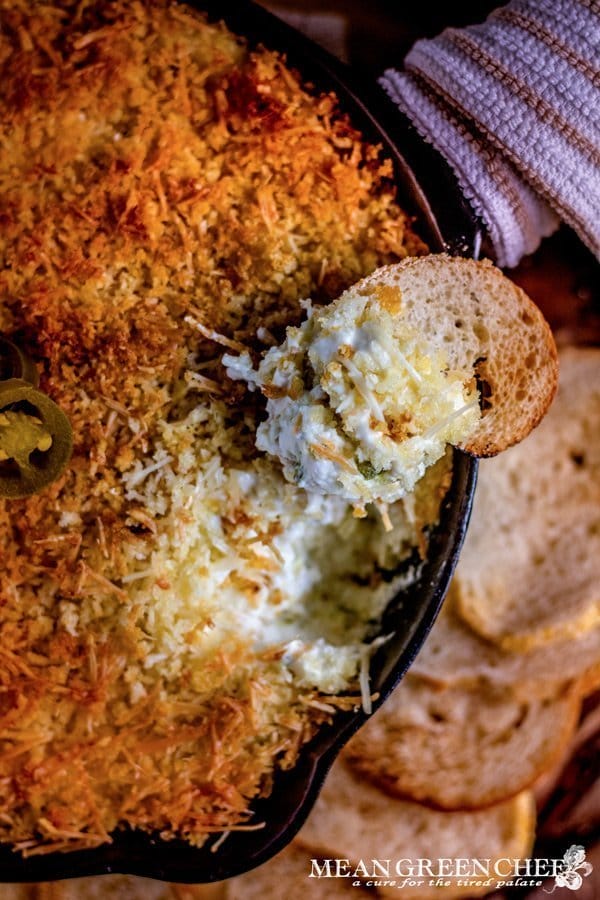 Overhead photo of Jalapeno Popper Dip in a cast iron pan surrounded with toasted sourdough bread rounds. on a rustic wooden background. Mean Green Chef