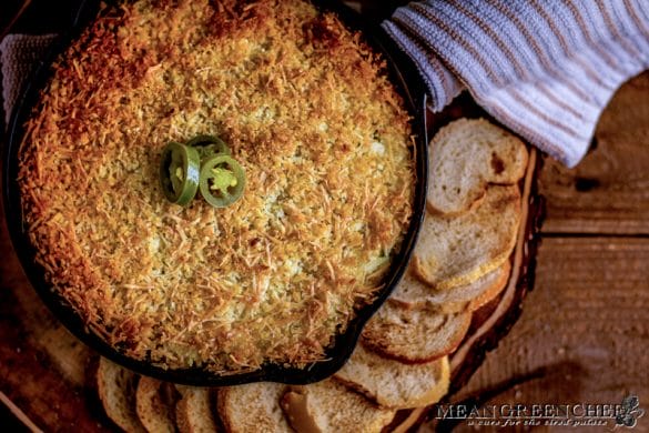 Overhead photo of Jalapeno Popper Dip in a cast iron pan surrounded with toasted sourdough bread rounds. on a rustic wooden background. Mean Green Chef