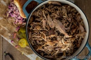 Overhead photo of Slow Roasted Pulled Pork in a gray Dutch Oven with sandwich off the the side in the background. Mean Green Chef