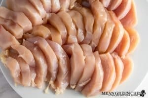 Raw chicken breast sliced into medallions, neatly arranged on a white plate, showcasing their fresh, pink flesh suitable for cooking.