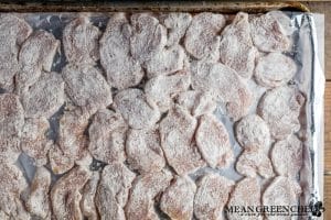 Sliced and floured seasoned chicken breast medallions arranged in rows on a parchment lined baking sheet. Resting to absorb the flour, prior to cooking.
