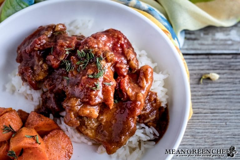 A bowl of Chicken Pierre coated in a rich tomato sauce, served over Jasmine rice. Garnished with fresh thyme, accompanied by a side of roasted carrots.