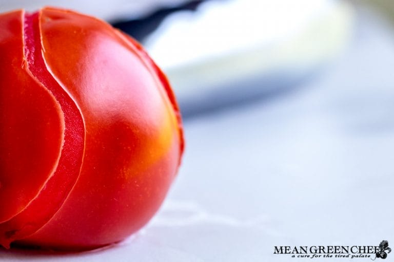 Close-up of a ripe blanched, glossy red tomato with soft-focus background, highlighting its vibrant color and fresh appearance. The skin is split in an artful pattern up the center in a wavy line, from being blanched.