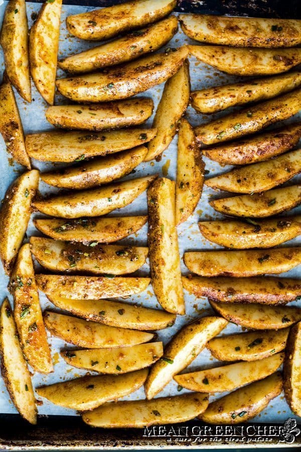 Sheet pan lined with parchment paper and potato wedges for Crispy Oven Fries.