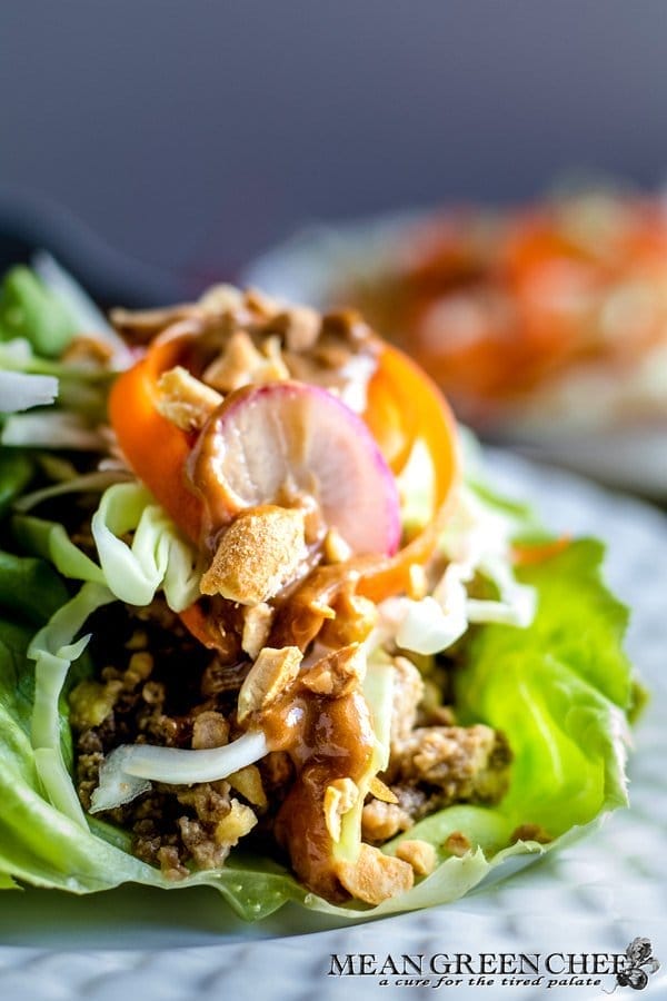A close-up image of a lettuce wrap filled with Larb, sliced radishes, prik nam pla, and topped with a drizzle of peanut sauce and crispy lettuce shreds.