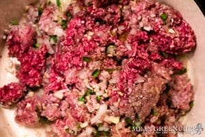 Raw ground beef and pork mixed with chopped onions and green herbs cooking in a skillet, close-up view. For making Larb for Thai Lettuce Wraps.
