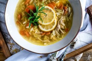 White bowl with a gold rim filled with Lemon Chicken Orzo Soup.