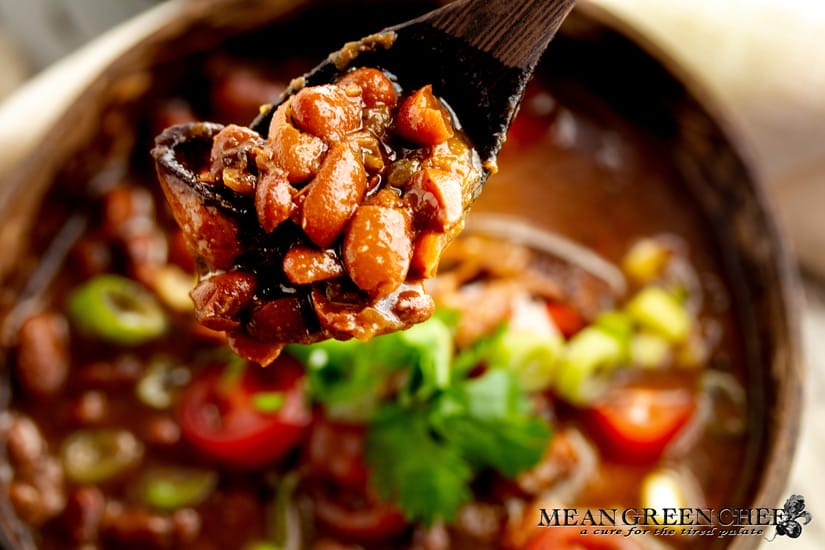 A wooden spoon lifting Slow Cooker Texas Pinto Beans from a rustic wooden bowl, showcasing vibrant colors and textures, steam rising warmly.