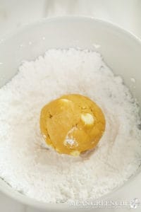Meyer Lemon Cookie Dough rolled into a ball for making a cookie and being rolled in a white bowl of powdered sugar.