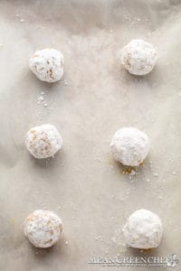Six powdered sugar-coated Meyer Lemon Cookies, evenly spaced on a parchment paper lined sheet pan. Ready to be baked.
